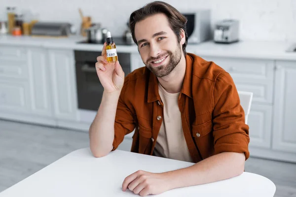 Smiling man holding cbd oil in kitchen — Stock Photo