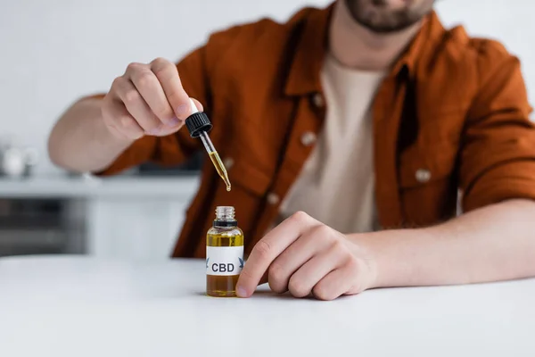 Обрезанный вид человека, держащего пипетку рядом с бутылкой масла CBD — стоковое фото