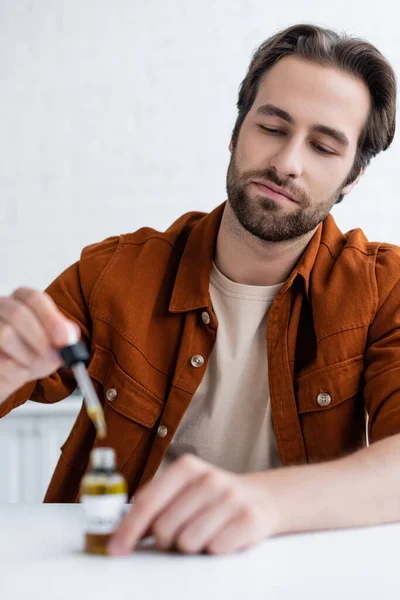 Hombre sosteniendo pipeta borrosa cerca de la botella de aceite de cbd - foto de stock