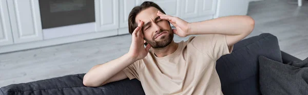 Homme souffrant de maux de tête sur le canapé à la maison, bannière — Photo de stock