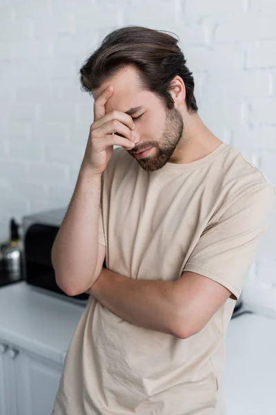 Hombre enfermo con los ojos cerrados de pie en la cocina - foto de stock