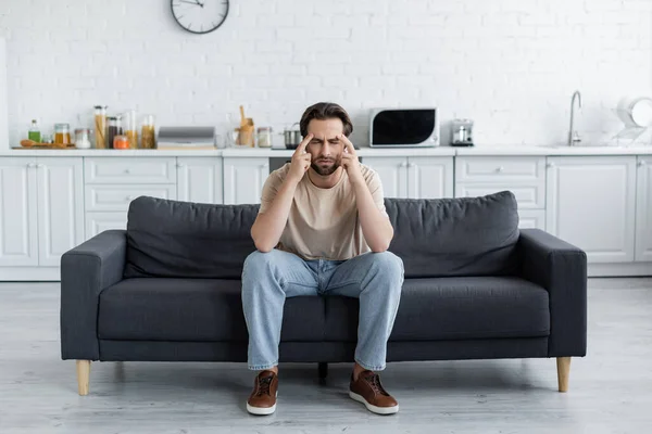 Homem sentado com os olhos fechados no sofá enquanto sofre de dor de cabeça — Fotografia de Stock