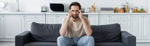 Hombre que sufre de dolor de cabeza en el sofá en la cocina, pancarta - foto de stock