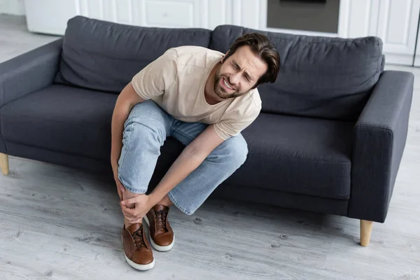 Mann leidet unter Schmerzen im Bein auf Couch — Stockfoto