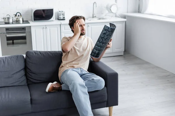 Müder Mann schaut auf Mri-Scan auf Couch — Stockfoto