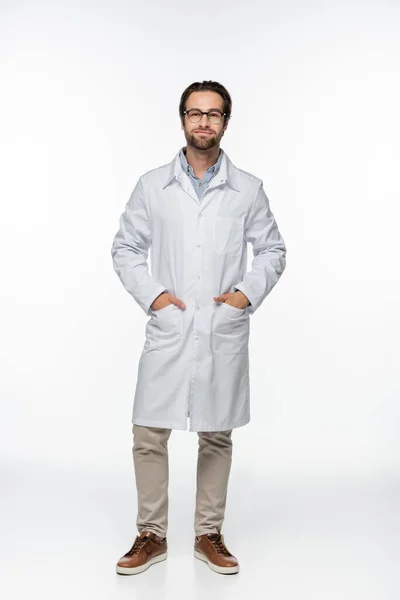 Doctor in eyeglasses and coat looking at camera on white background — Stock Photo