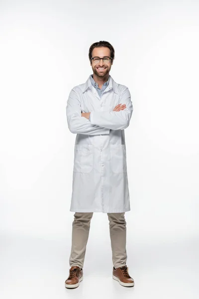 Médico sorridente com braços cruzados olhando para a câmera no fundo branco — Fotografia de Stock