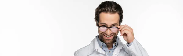 Doctor holding eyeglasses while smiling at camera isolated on white, banner — Stock Photo