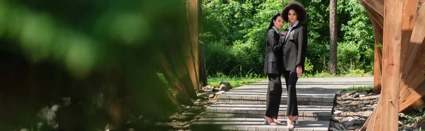 Interracial lesbian couple looking at camera under arch, banner — Stock Photo