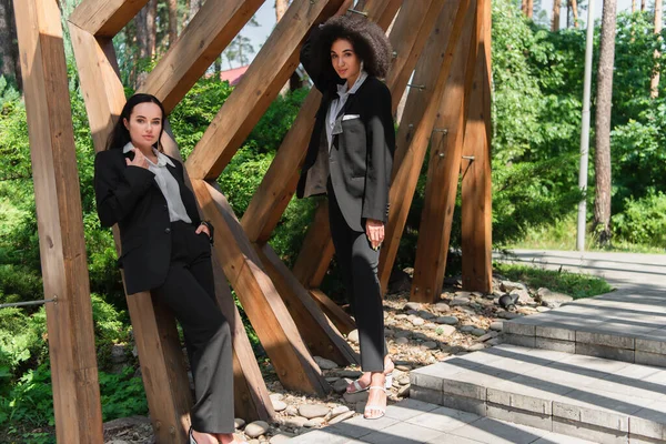 Interracial same sex couple in suits standing near arch in park — Stock Photo