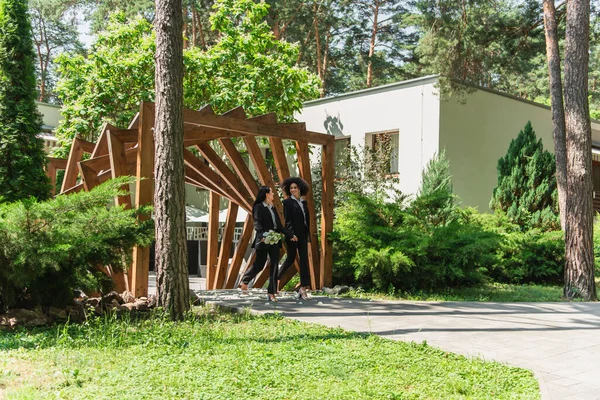 Exotisches lesbisches Paar mit Hochzeitsstrauß spazieren im Park — Stockfoto