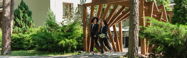 Couple homosexuel multiethnique avec bouquet de mariage marchant dans le parc, bannière — Photo de stock