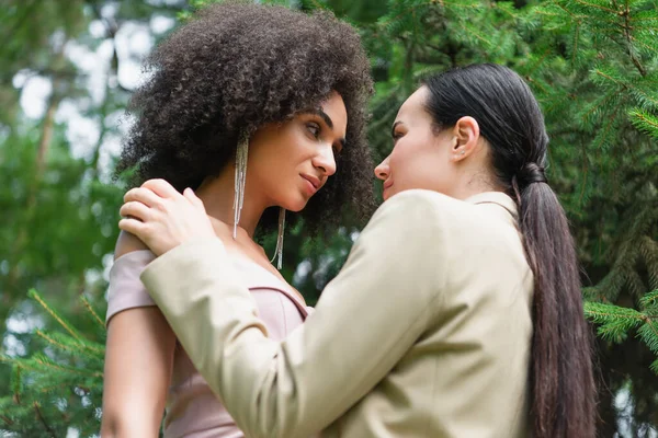 Low angle view of lesbian woman hugging african american girlfriend in dress in park — Stock Photo