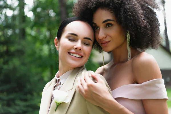 African american woman in dress hugging smiling girlfriend in suit — Stock Photo