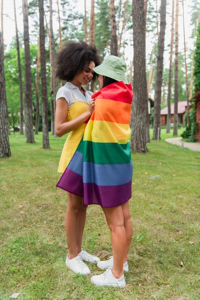 Positiva africana americana mujer abrazando novia en lgbt bandera en parque - foto de stock