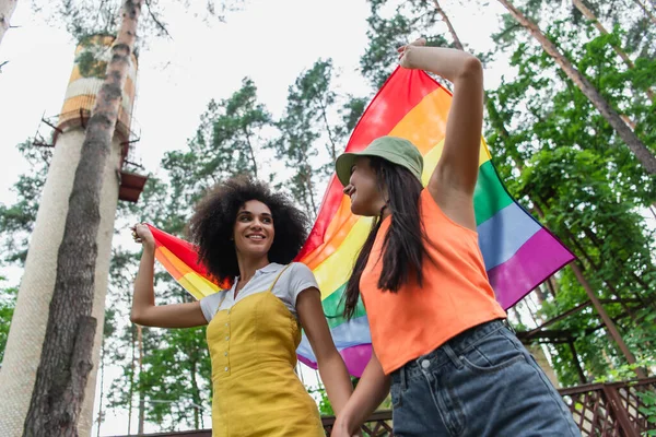 Ângulo baixo vista de interracial mesmo sexo casal segurando lgbt bandeira ao ar livre — Fotografia de Stock