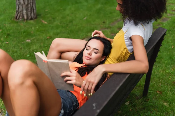 Jeune femme lisant un livre près de la petite amie afro-américaine dans le parc — Photo de stock