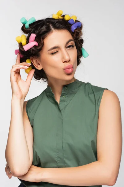 Young woman with colorful hair curlers pouting lips isolated on grey — Stock Photo