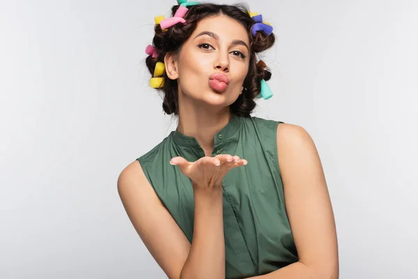 Mujer joven con rizadores de pelo de colores enviando beso de aire aislado en gris - foto de stock