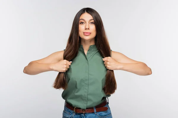 Jovem mulher ajustando o cabelo brilhante e olhando para a câmera isolada no cinza — Fotografia de Stock