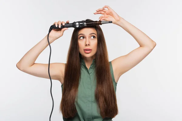 Giovane donna utilizzando arricciacapelli isolato su grigio — Foto stock