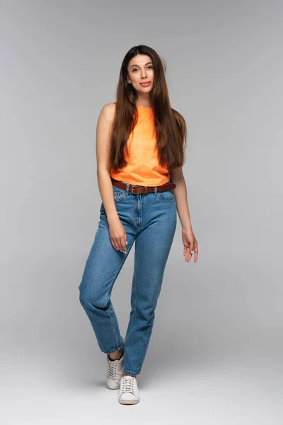 Full length of smiling young woman in denim jeans posing on grey — Stock Photo