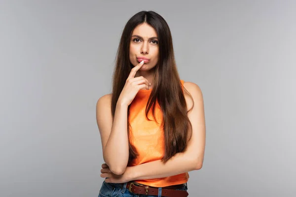 Mujer pensativa con el pelo largo mirando a la cámara aislada en gris - foto de stock