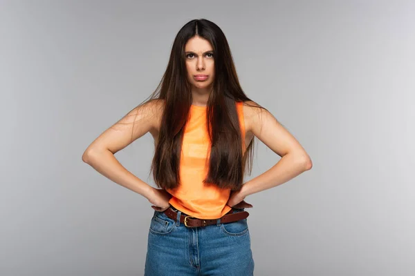 Mujer disgustada con el pelo largo de pie con las manos en las caderas aisladas en gris - foto de stock