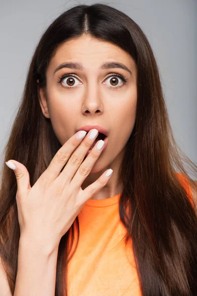 Shocked young woman covering mouth isolated on grey — Stock Photo