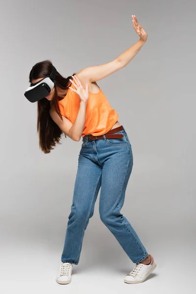 Full length of scared young woman in vr headset gesturing on grey — Stock Photo