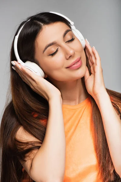 Mujer sonriente en auriculares inalámbricos escuchando música aislada en gris - foto de stock