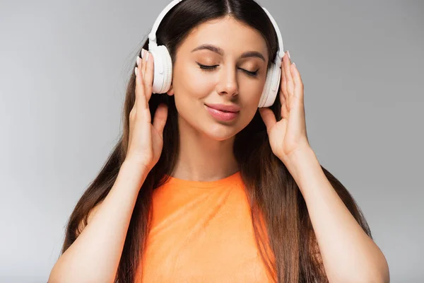 Молода жінка в бездротових навушниках слухає музику і посміхається ізольовано на сірому — стокове фото