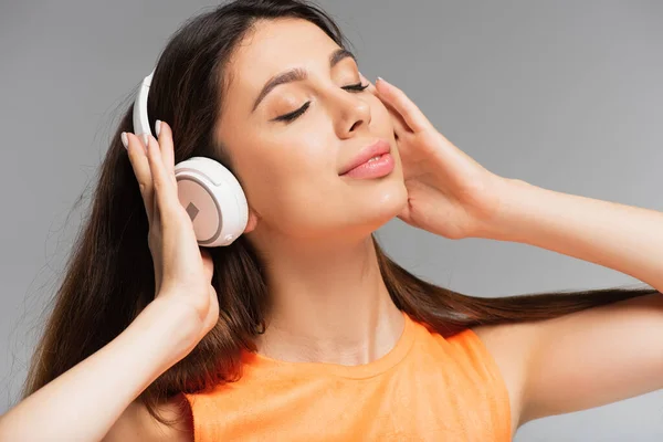 Pleased young woman in wireless headphones listening music isolated on grey — Stock Photo