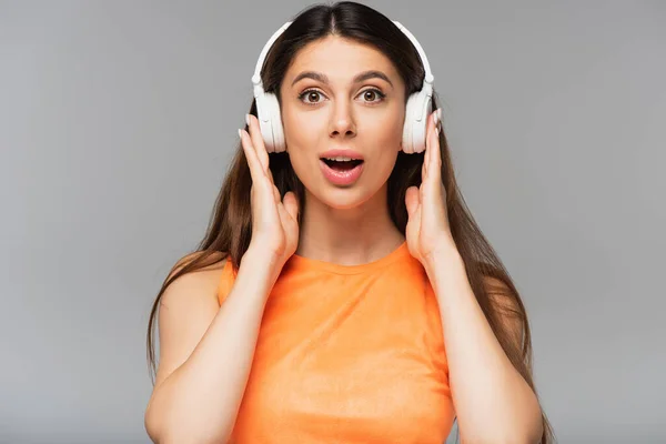 Überraschte junge Frau mit drahtlosen Kopfhörern, die isoliert auf grau Musik hört — Stockfoto