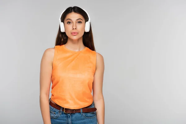 Jolie jeune femme en écouteurs sans fil écouter de la musique isolée sur gris — Photo de stock