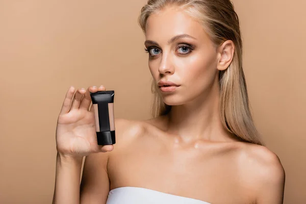 Young woman with perfect skin holding face foundation isolated on beige — Stock Photo