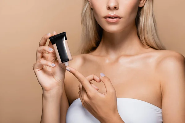 Cropped view of woman with bare shoulders applying face foundation on finger isolated on beige — Stock Photo