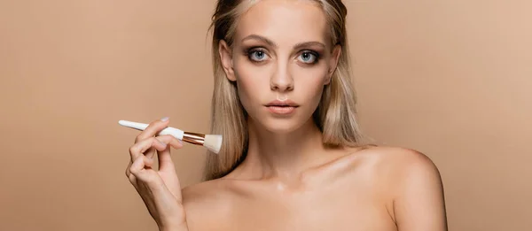 Young woman with cosmetic brush looking at camera isolated on beige, banner — Stock Photo