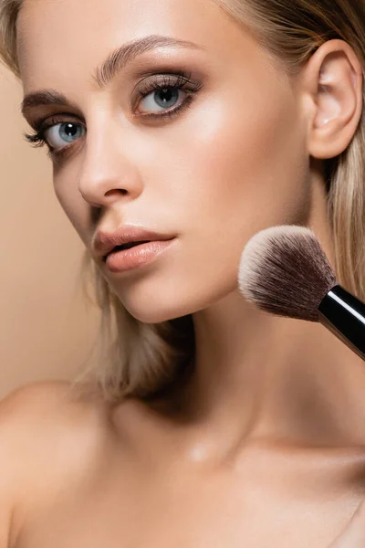 Close up view of woman with perfect skin powdering face with soft cosmetic brush isolated on beige — Stock Photo