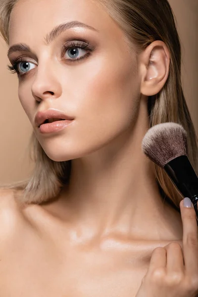 Young woman with clean skin and grey eyes posing with large cosmetic brush isolated on beige — Stock Photo