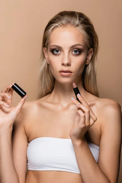 Blonde woman with perfect skin holding lipstick isolated on beige — Stock Photo