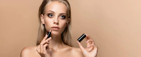 Blonde woman with grey eyes holding lipstick isolated on beige, banner — Stock Photo