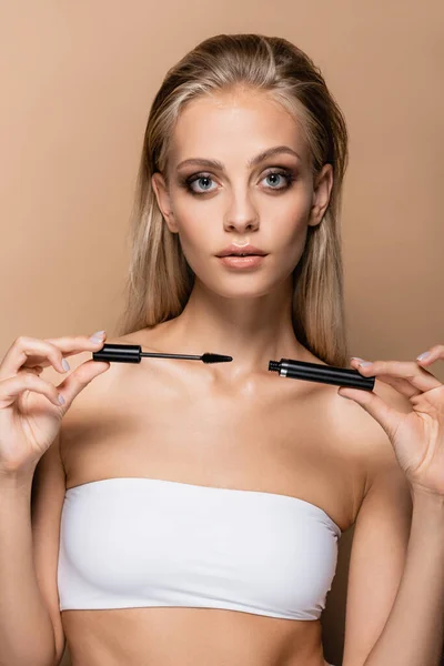 Jeune femme avec maquillage montrant mascara noir isolé sur beige — Photo de stock