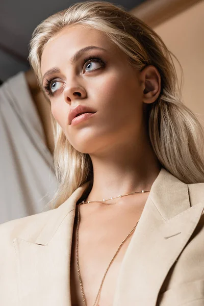 Tiefansicht einer blonden Frau in goldener Halskette in der Nähe von Vorhängen auf Beige — Stockfoto