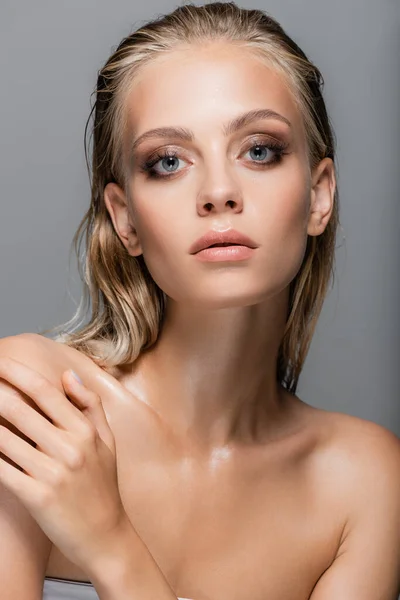 Femme humide avec peau parfaite regardant caméra tout en touchant épaule nue isolé sur gris — Photo de stock