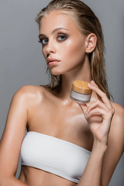 Bonita mujer con piel húmeda celebración crema cosmética aislada en gris - foto de stock