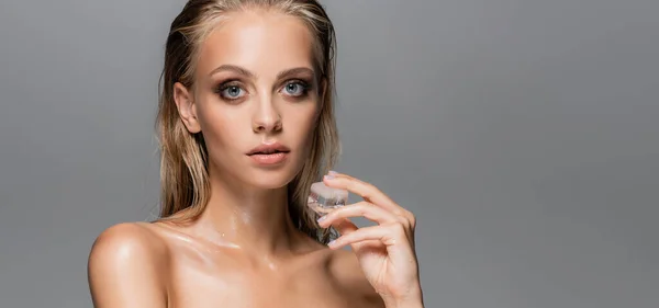 Mujer mojada con piel perfecta sosteniendo cubo de hielo aislado en gris, bandera - foto de stock