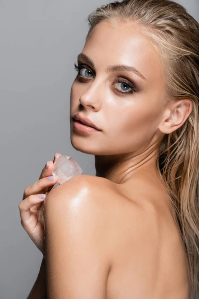 Sensual woman touching bare shoulder with ice cube isolated on grey — Stock Photo