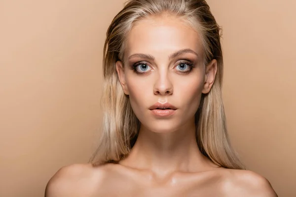 Blonde woman with makeup and naked shoulders looking at camera isolated on beige — Stock Photo