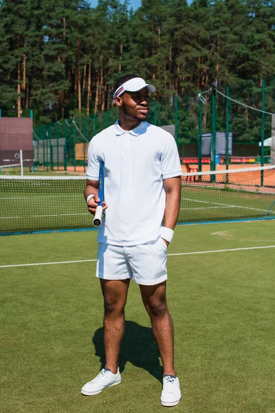 Deportista afroamericano sosteniendo raqueta de tenis y mano en bolsillo en la cancha - foto de stock